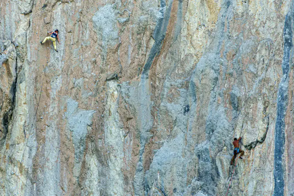 Climber on a steep rock face wearing bright technical apparel